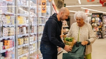 man helpt oudere vrouw met haar boodschappen in de supermarkt