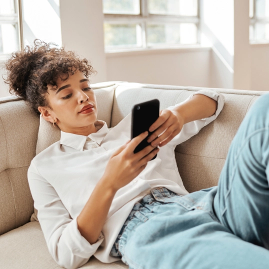 Jonge vrouw scrollend op haar smartphone in de zetel
