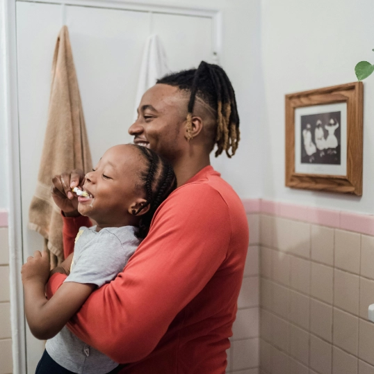 un papa et son enfant se brossent les dents en riant