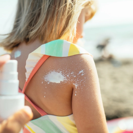 iemand smeert zonnecrème op rug van kind op het strand