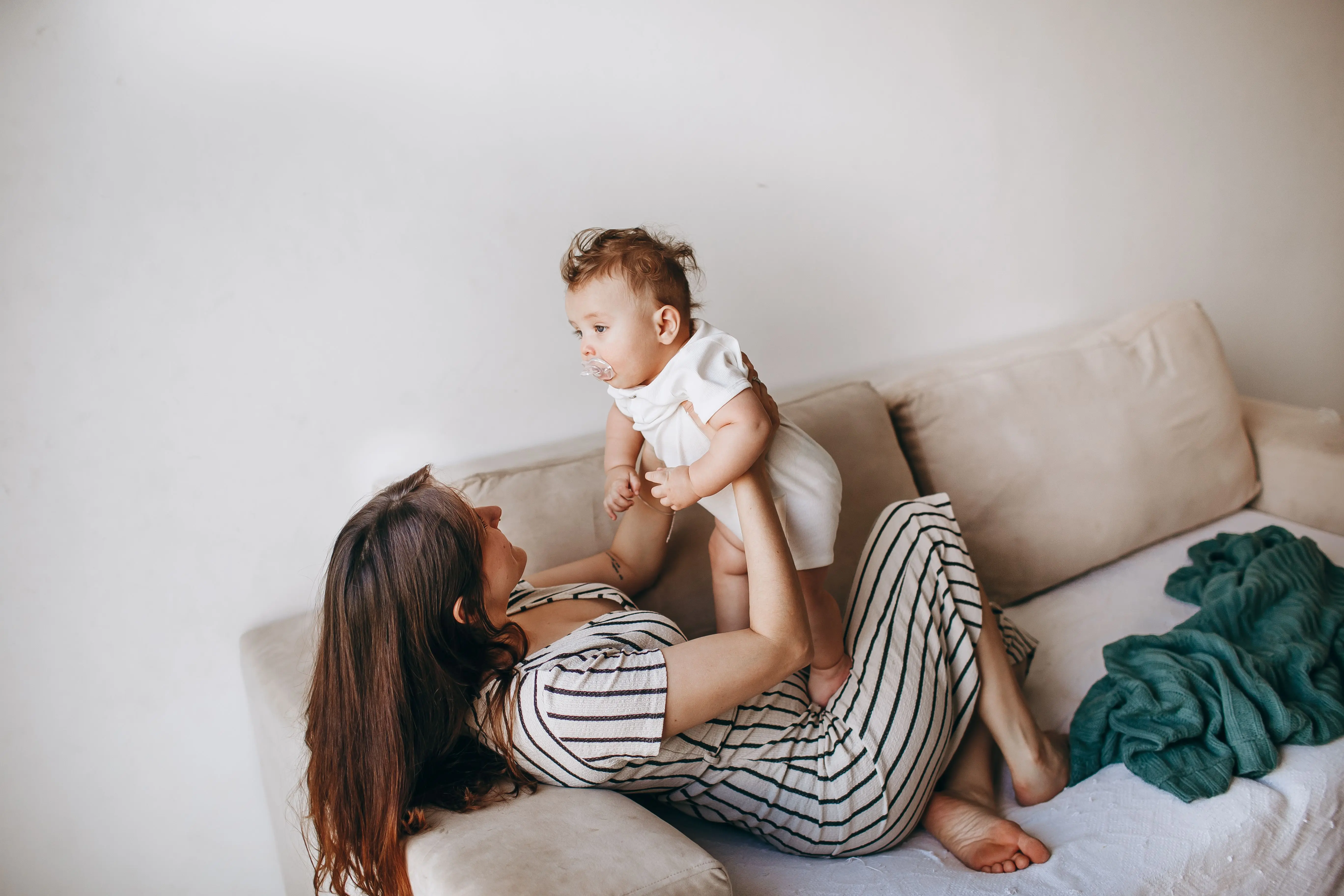 moeder ligt in zetel en houdt haar baby in de lucht