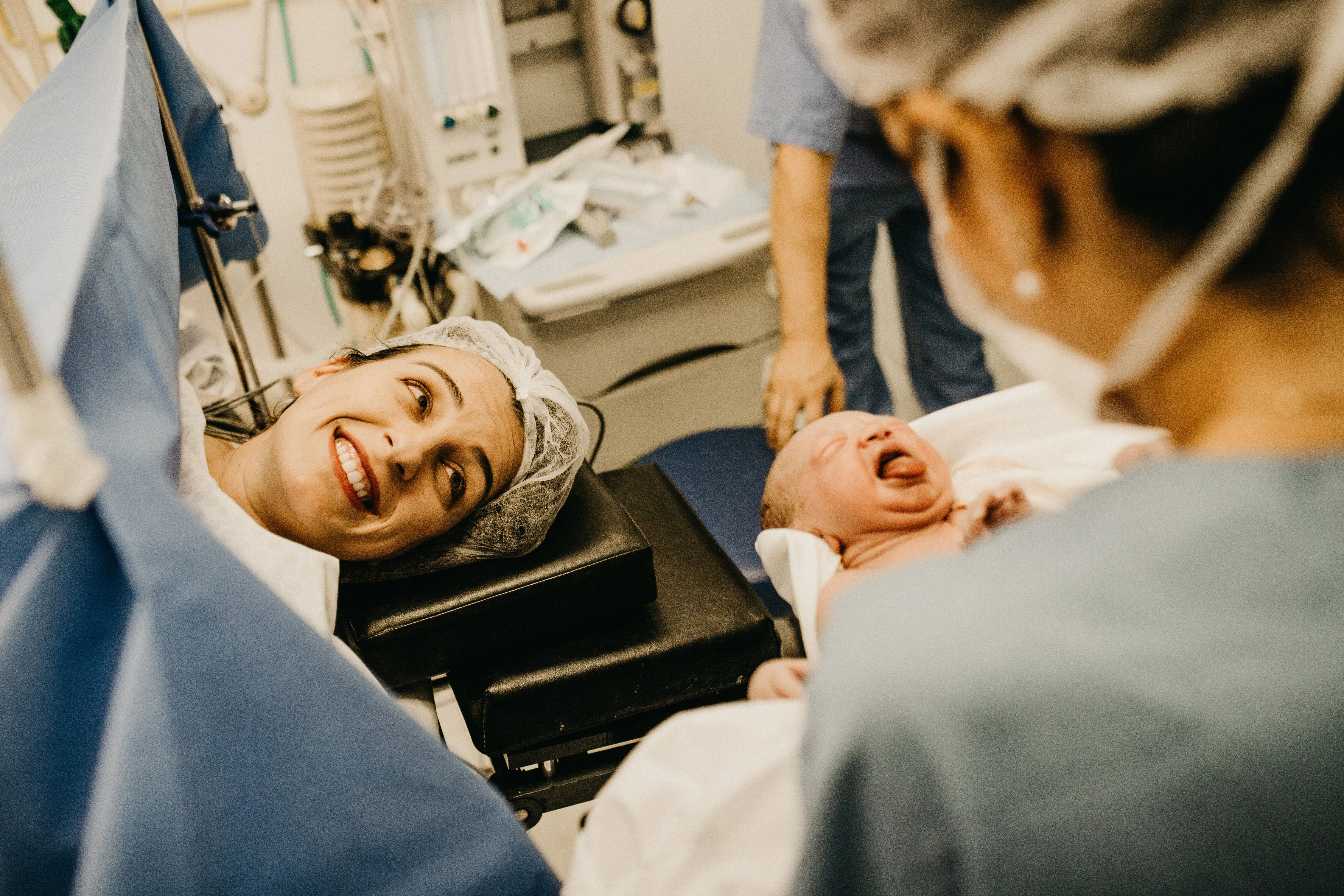 vrouw ligt op operatietafel en vroedvrouw houdt pasgeboren baby vast